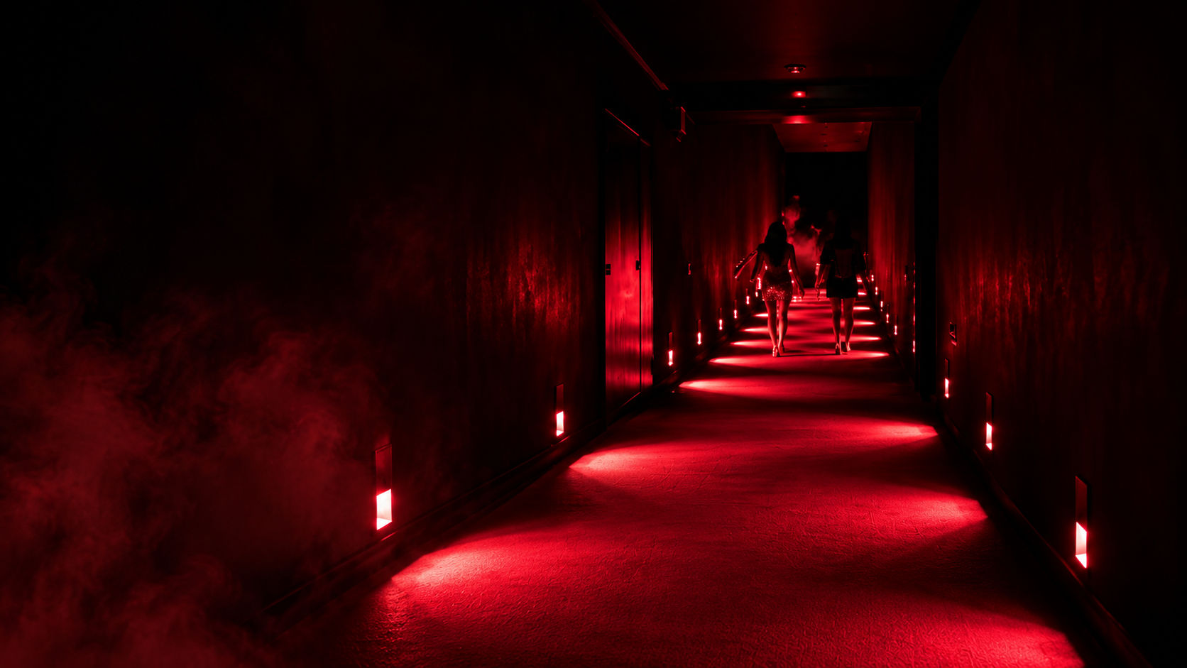 Two figures walking a red-lit corridor